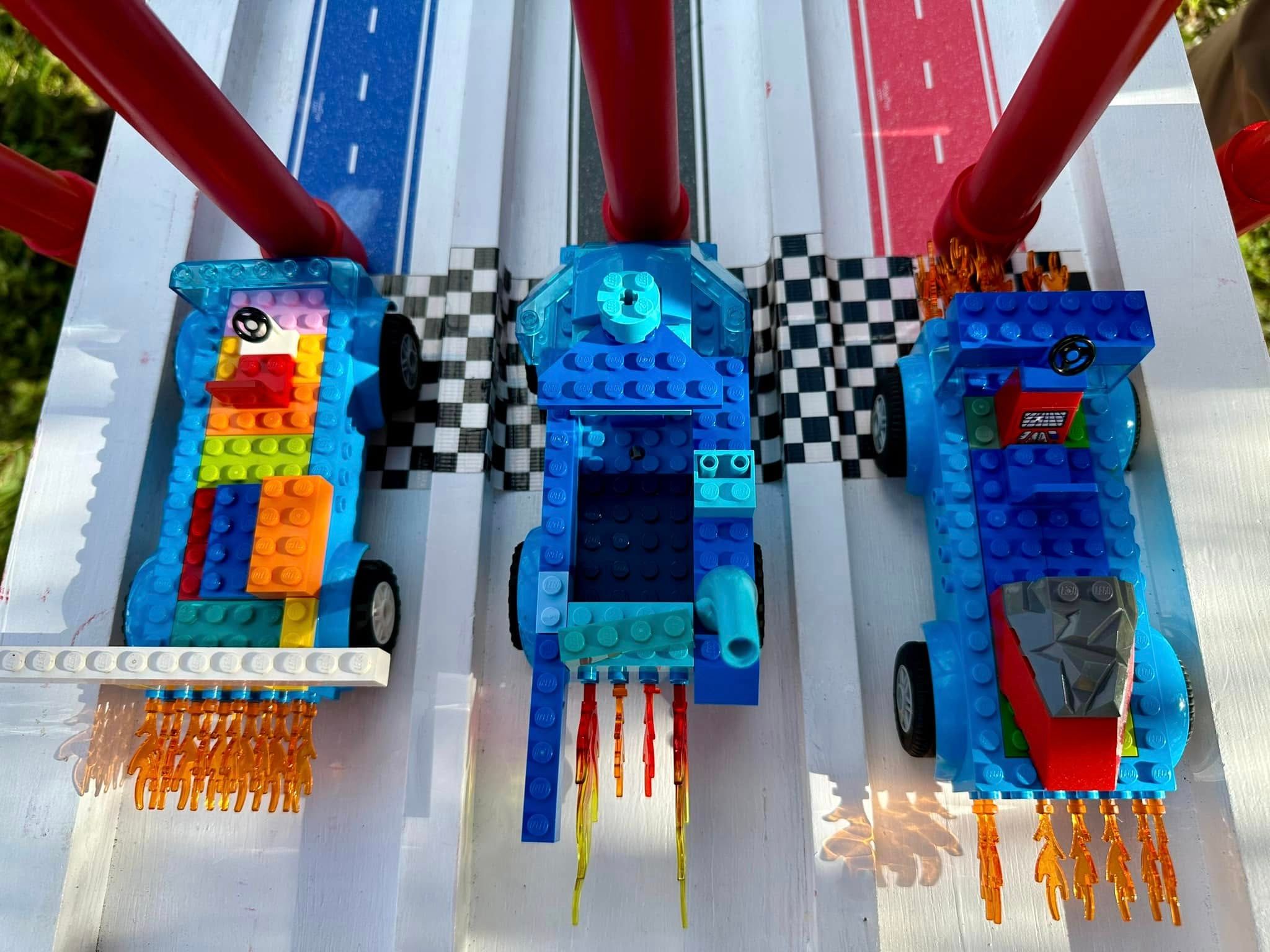 Three blue brick cars with flame pieces lined up at the checkered start of the Derby ramp