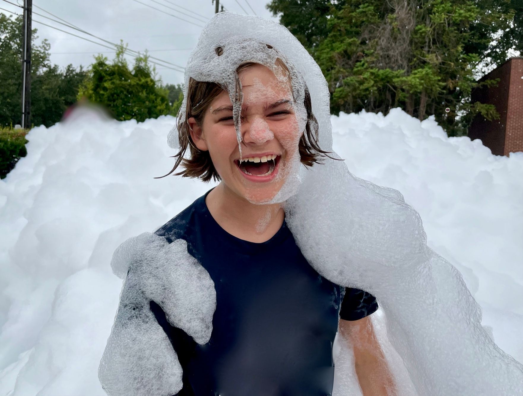 Kid at a foam birthday party, smiling with foam on his head