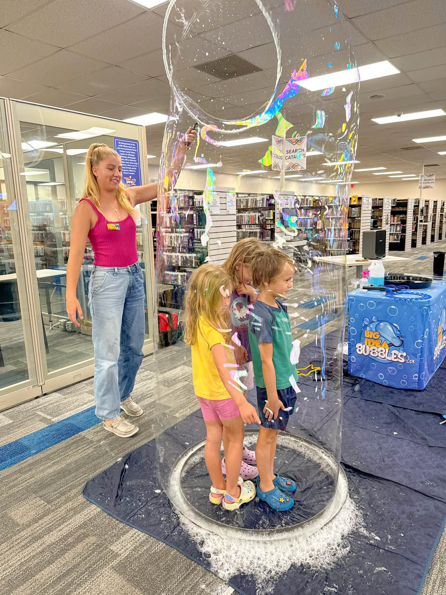 a child standing inside a giant bubble beside a host