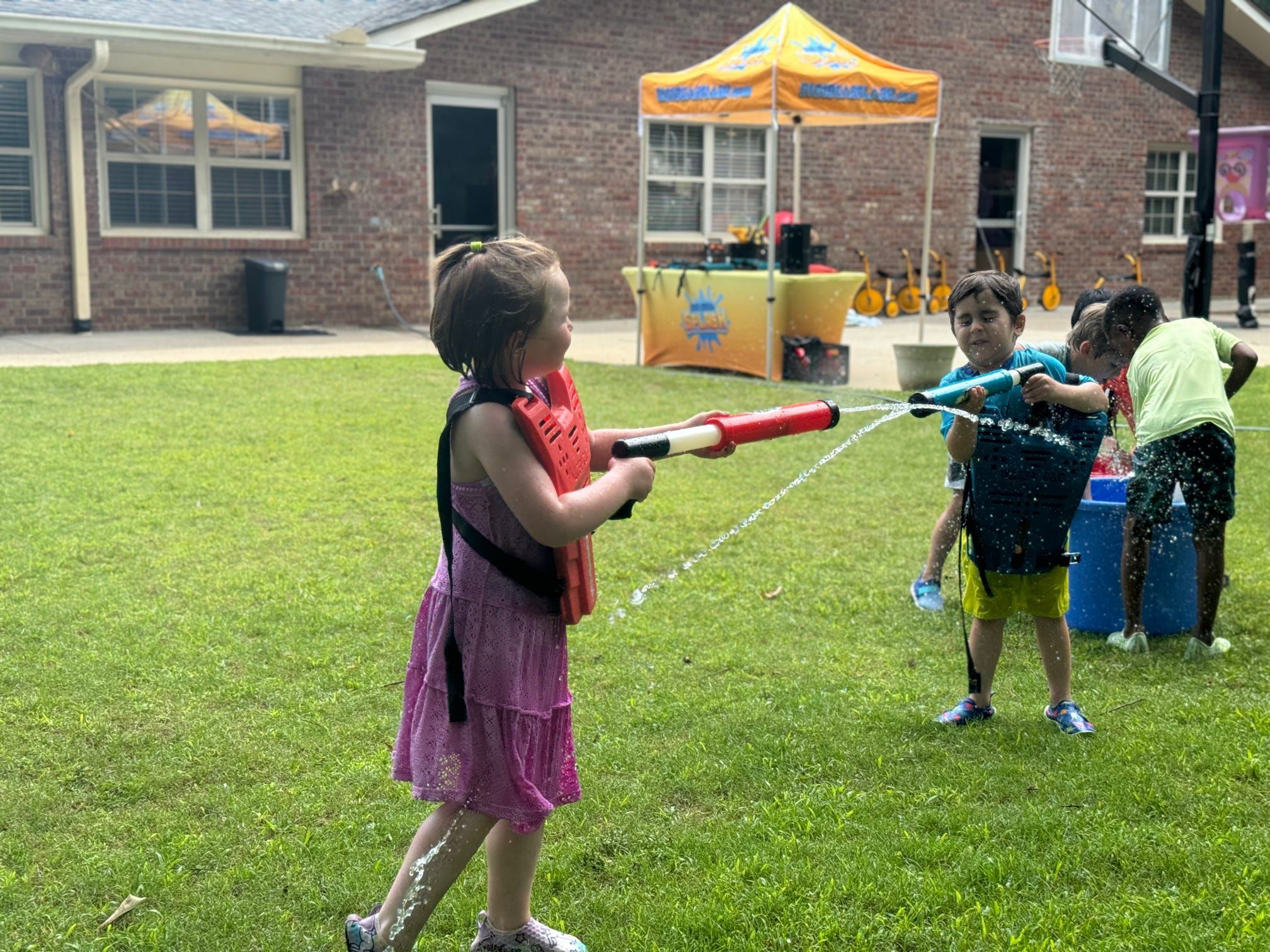 Two kids trade water blasts across a backyard lawn