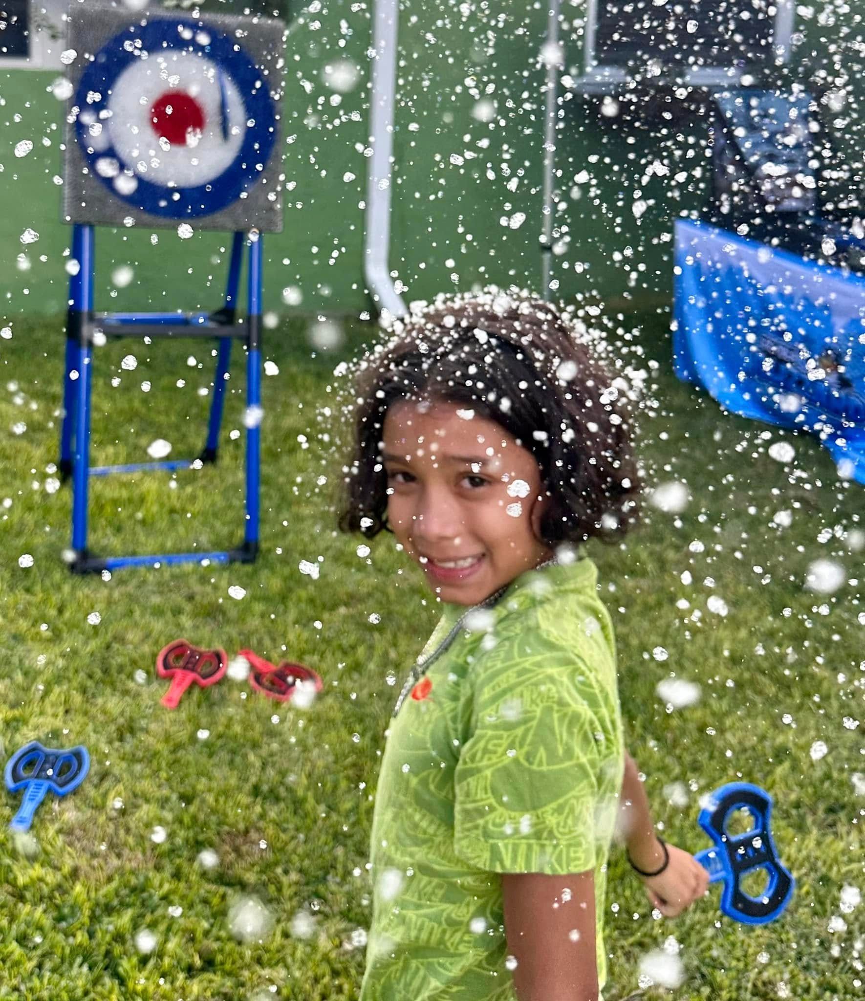 A boy covered in snow holds a soft throwing axe in front of the target