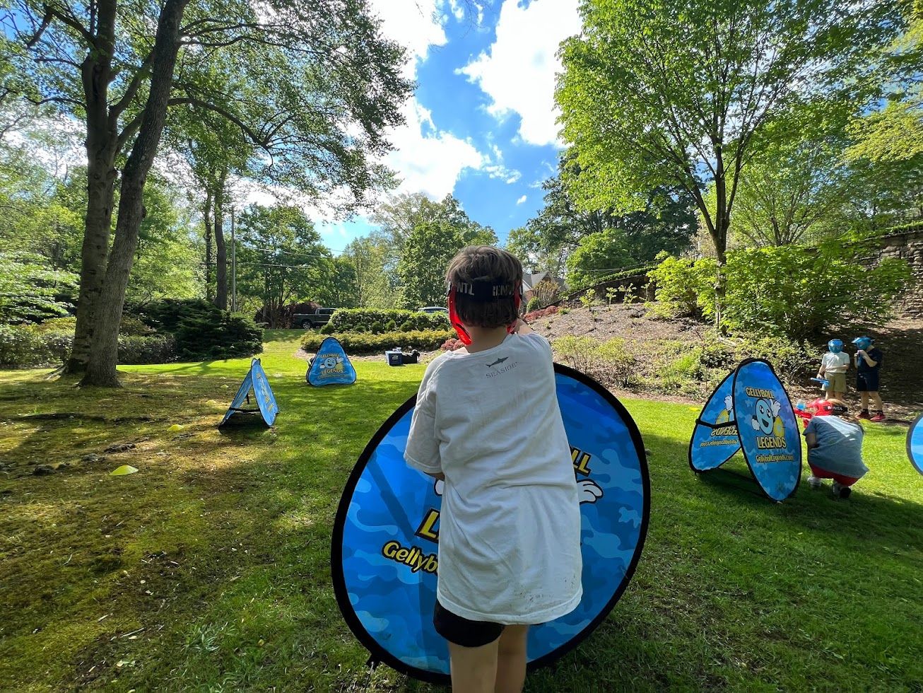 Kids spread out among pop-up bunkers on a sunny lawn during a game