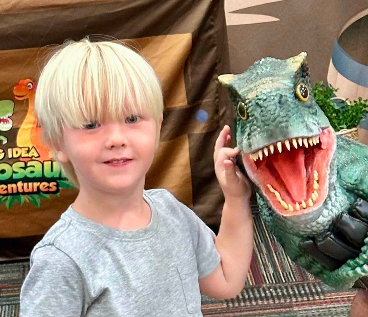 A grinning boy leans in next to a roaring lifelike baby T. rex