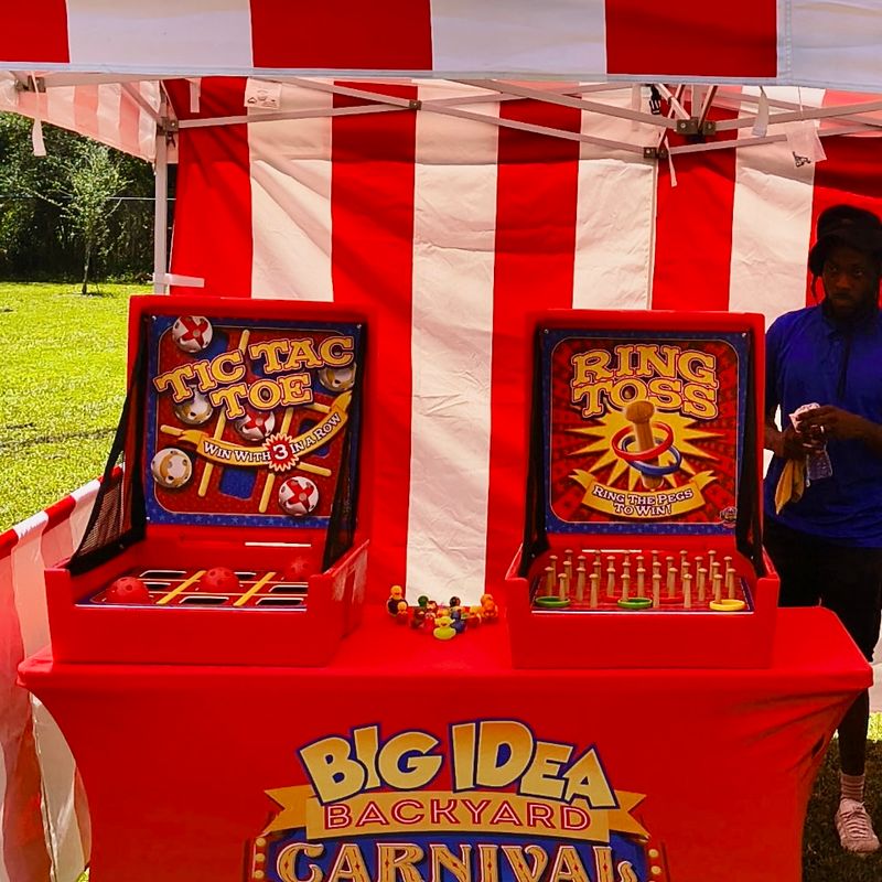 tic-tac-toe and ring toss game boards on a branded carnival table under a striped tent.