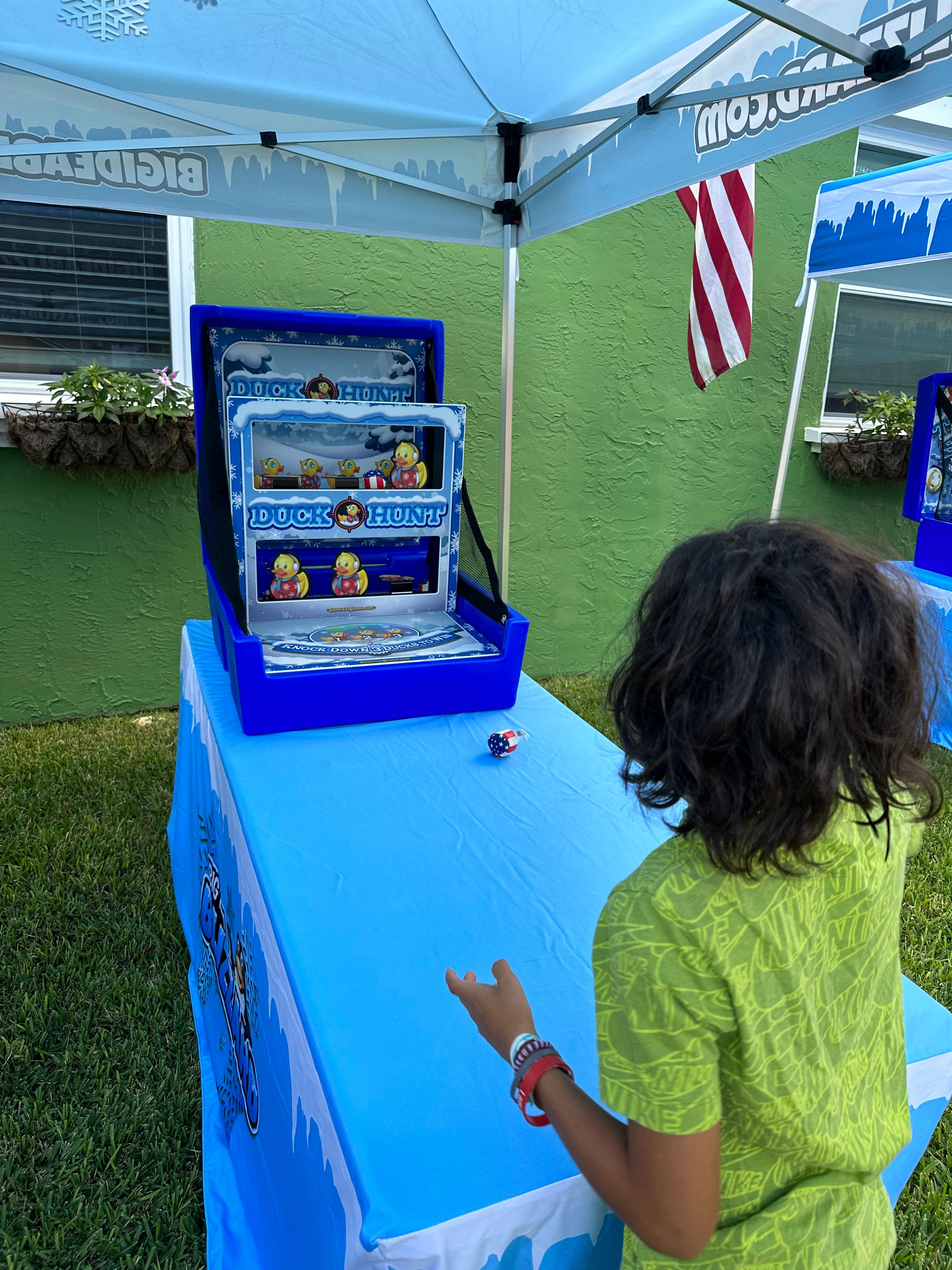 A boy throws a beanbag at the Duck Hunt game under a Blizzard tent