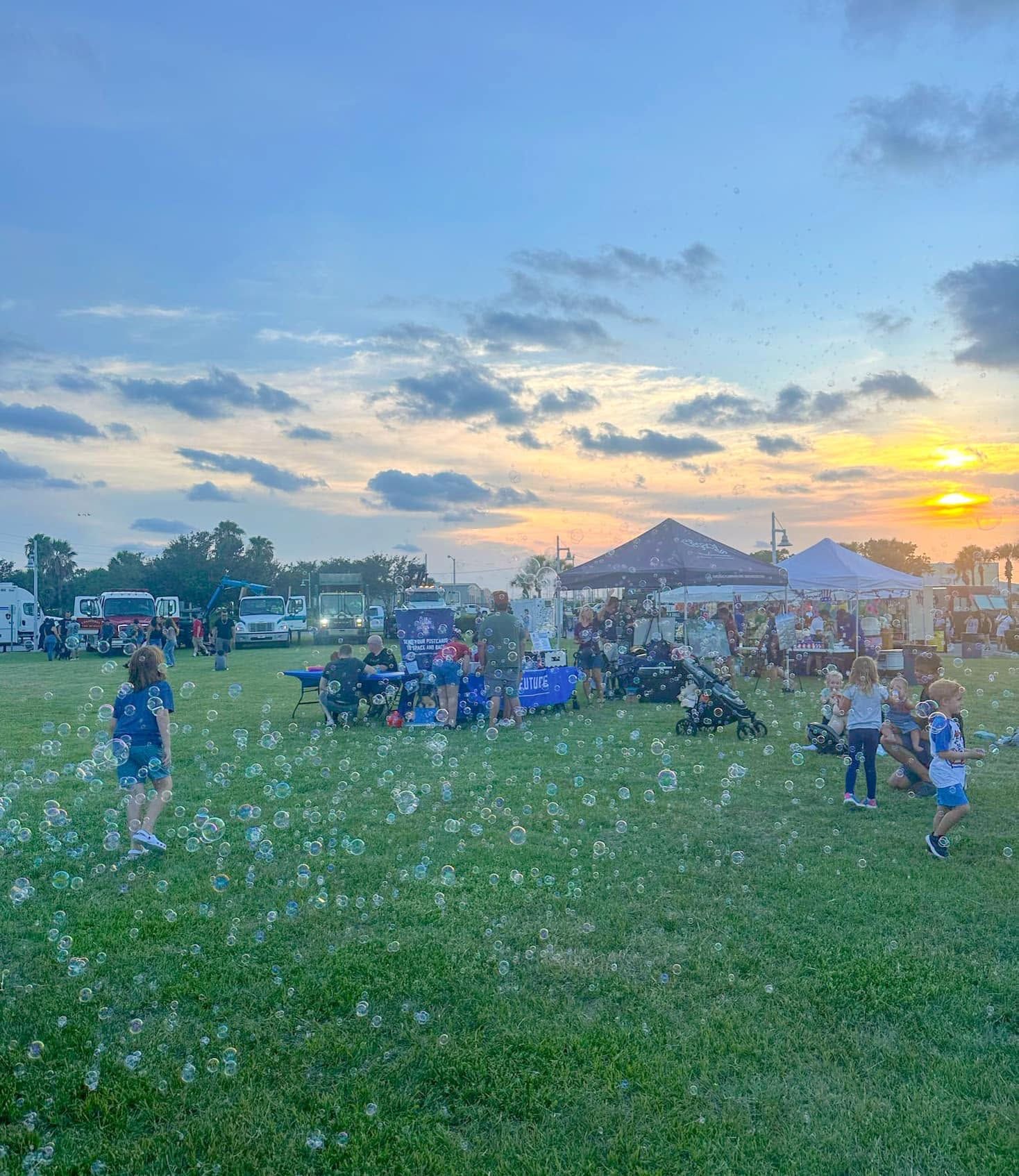 a bubble station on a festival lawn at sunset with an event tent behind it