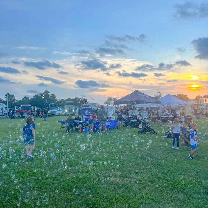 a bubble station on a festival lawn at sunset with an event tent behind it