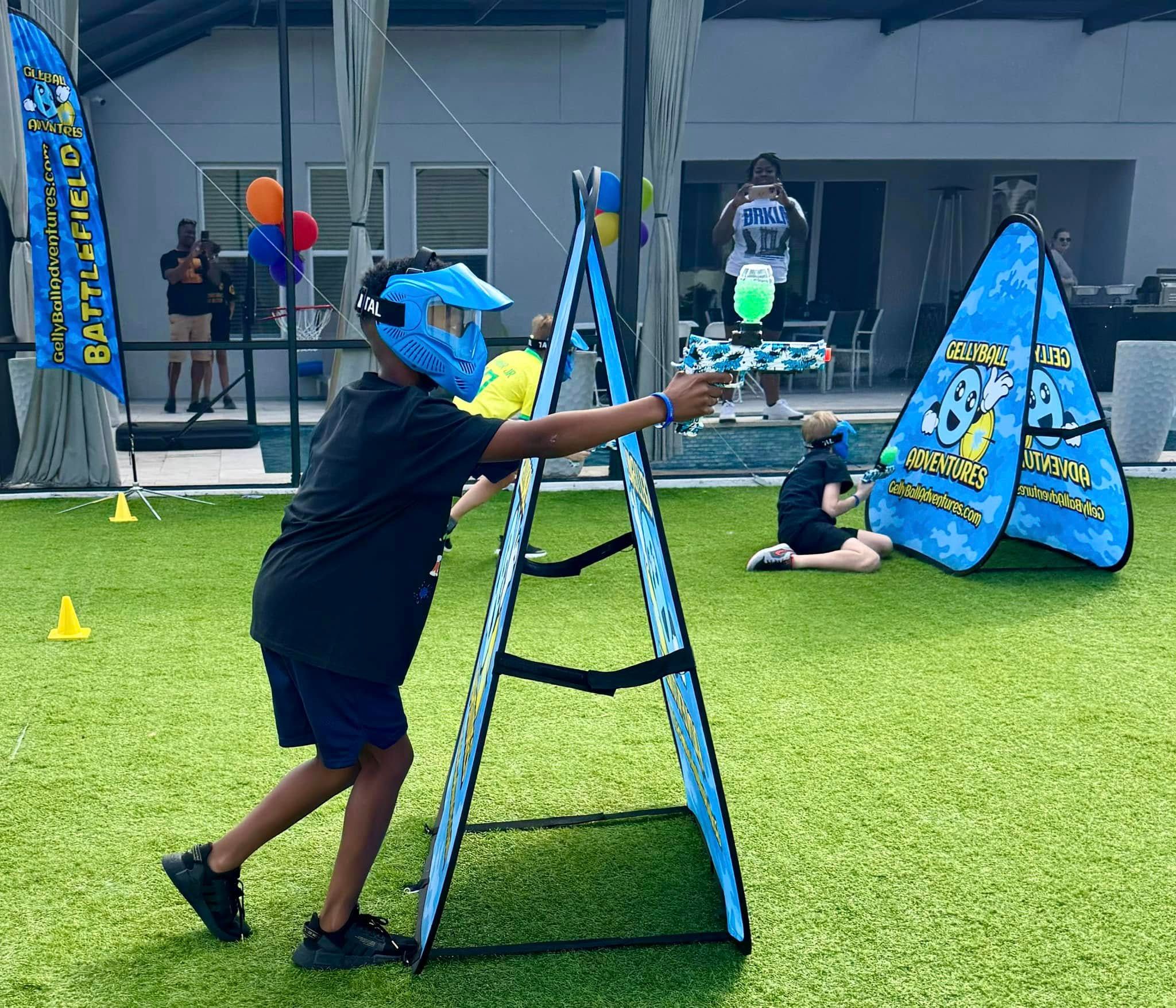 A boy in a mask aims around an A-frame bunker at a backyard birthday party