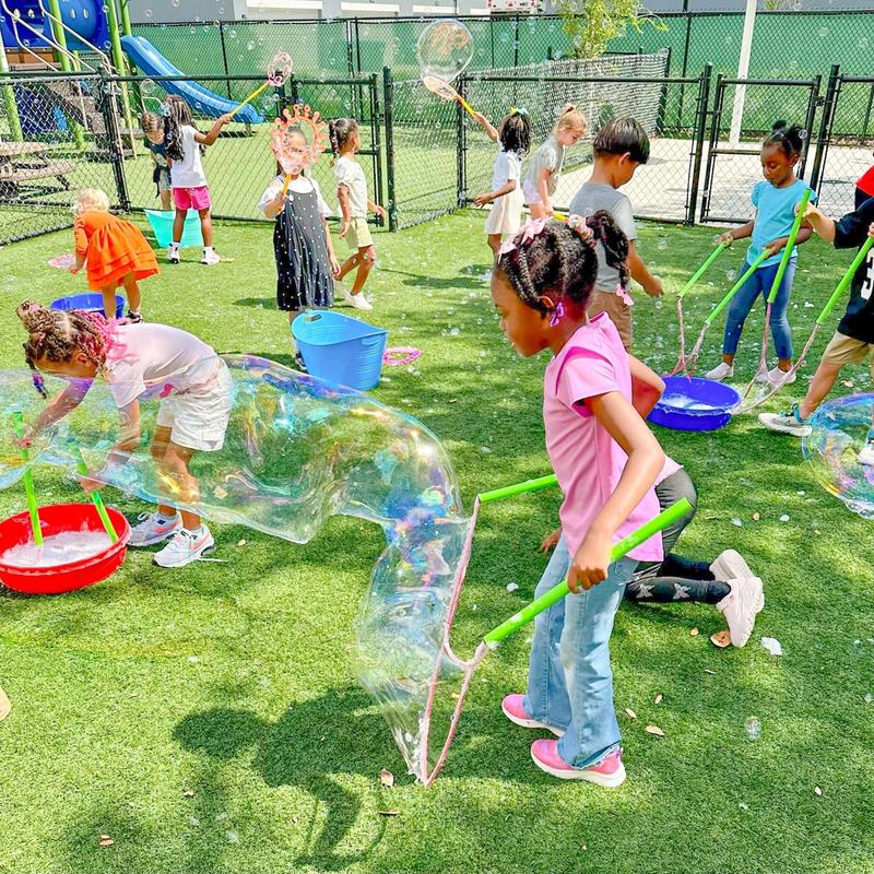 kids with wands chasing giant bubbles on a school playground