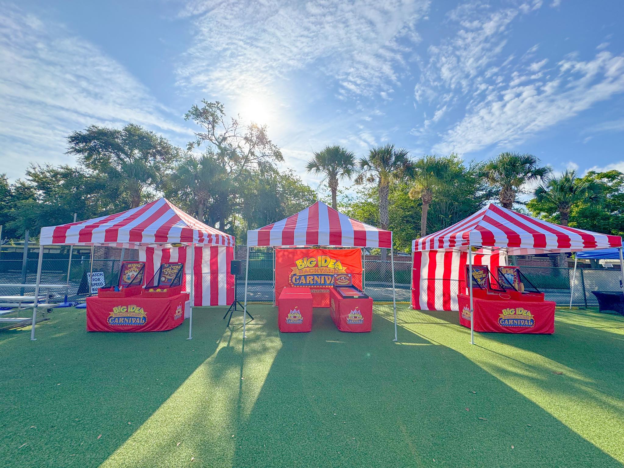 Three striped tents and eight classic carnival games setup for an event.