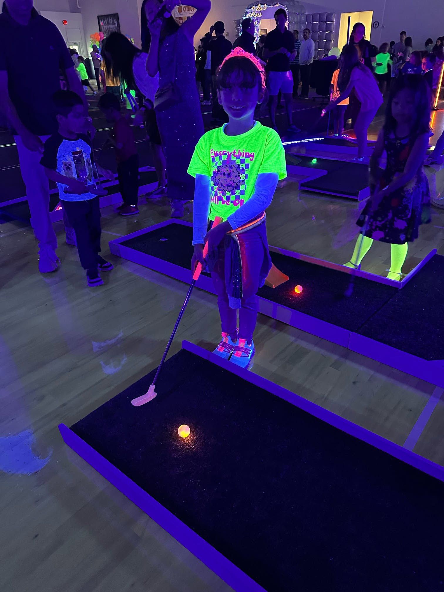a girl in a neon shirt putting on a blacklit mini golf hole