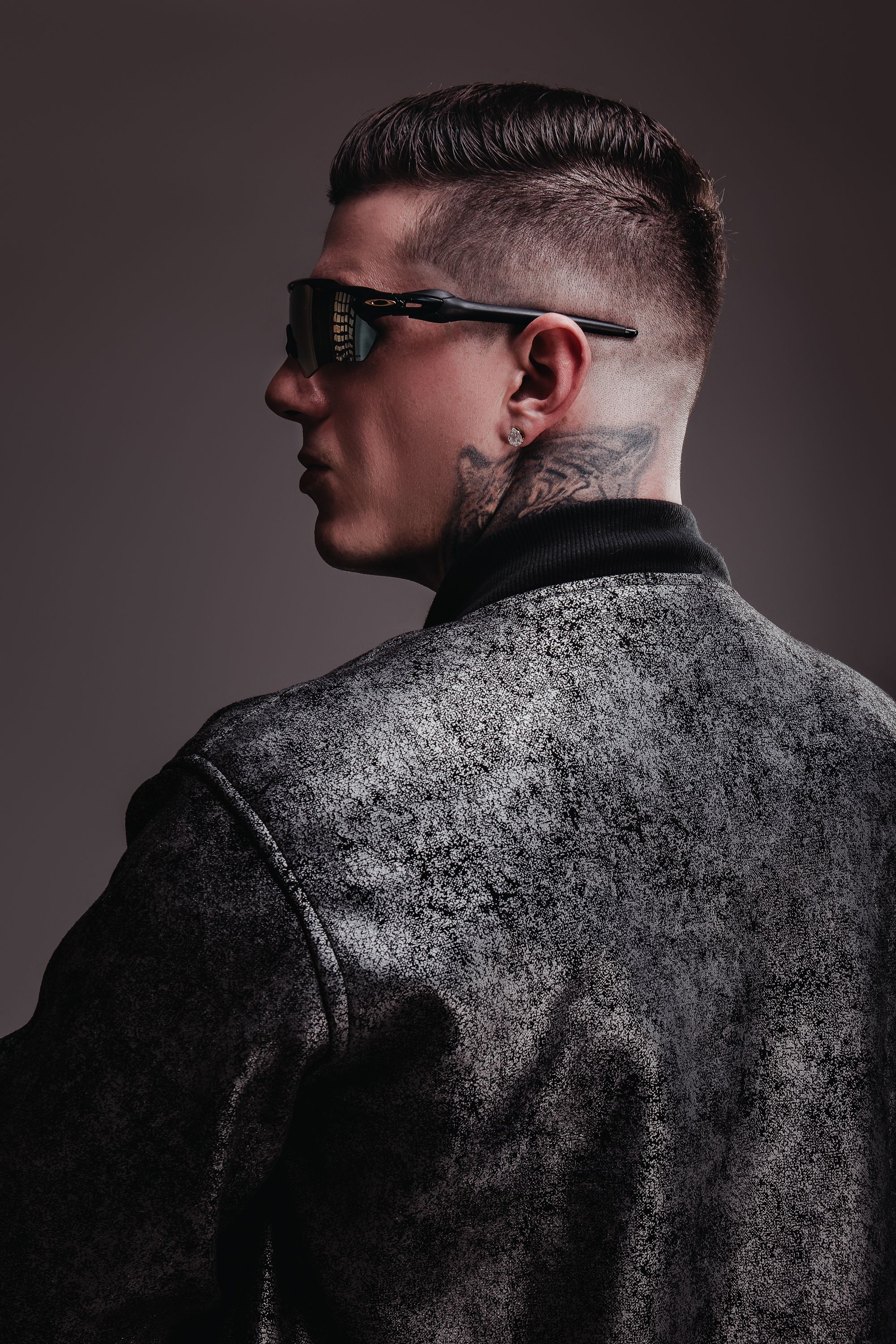 DJ Caio Moreira de costas, olhando de perfil, com jaqueta de couro