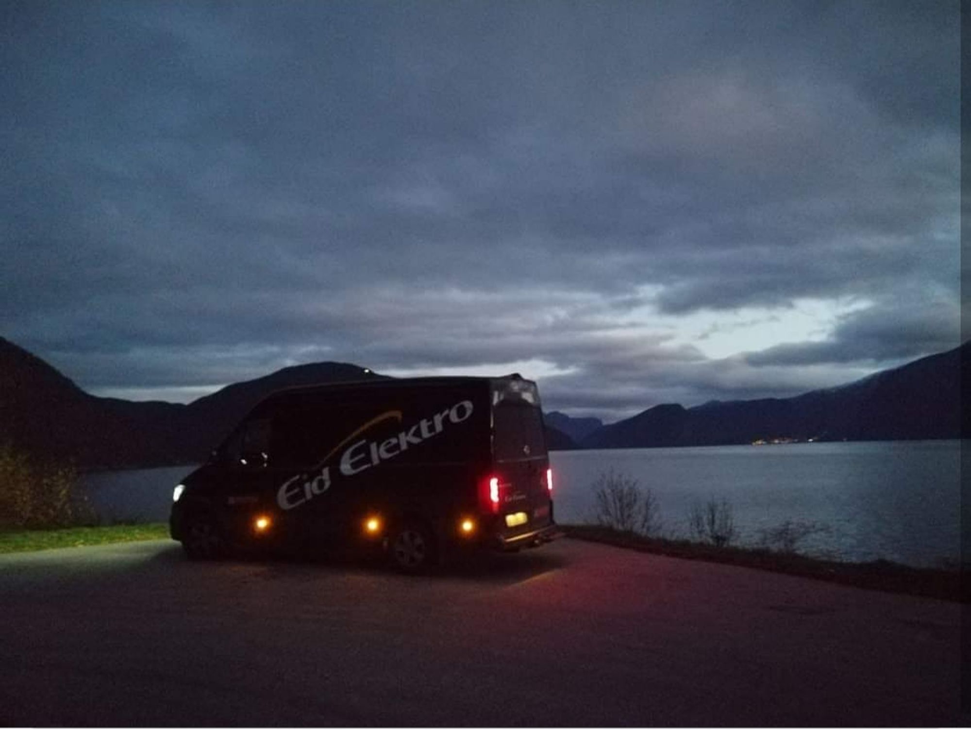 Eid Elektro bil med en fjord i bakgrunnen, det er mørkt ute.