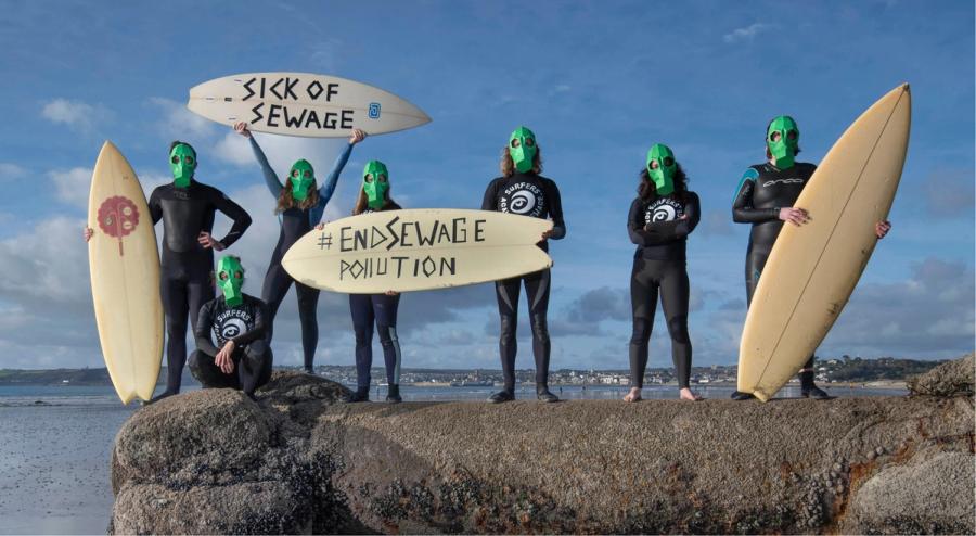 Surfers Against Sewage campaigners in green masks holding surfboards calling to end sewage pollution.
