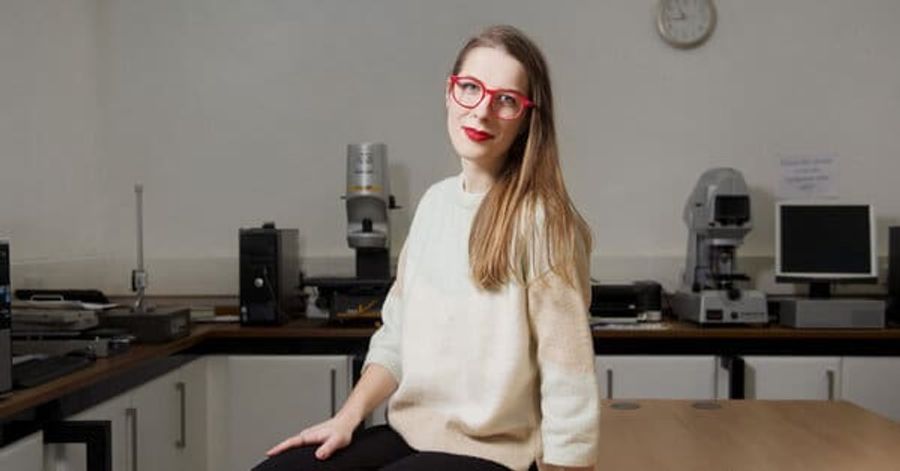 Woman with glasses seated on table with long brown hair and white sweater