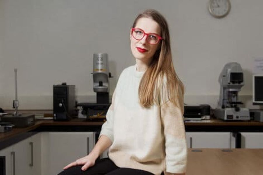 Woman with glasses seated on table with long brown hair and white sweater