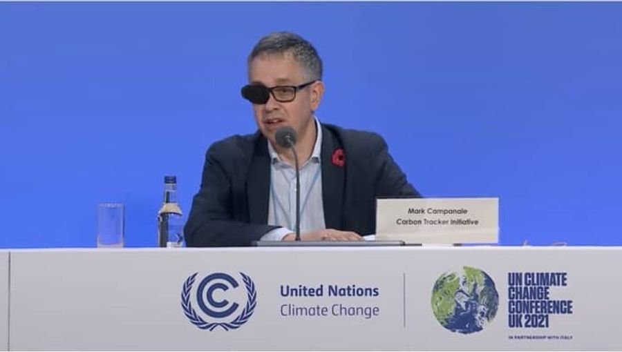 A white person in a suit sits at a conference table at COP26.