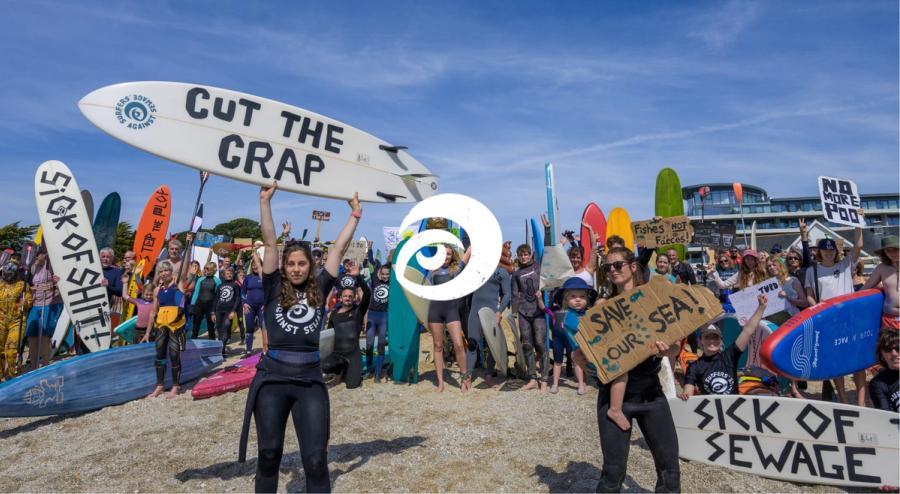 Surfers Against Sewage community campaigners and surfers holding boards with anti-sewage pollution messages at a coastal protest.