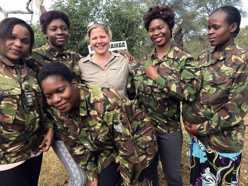 Holly Budge stands outside with members of the Black Mambas female rangers, who wear camouflage jackets.