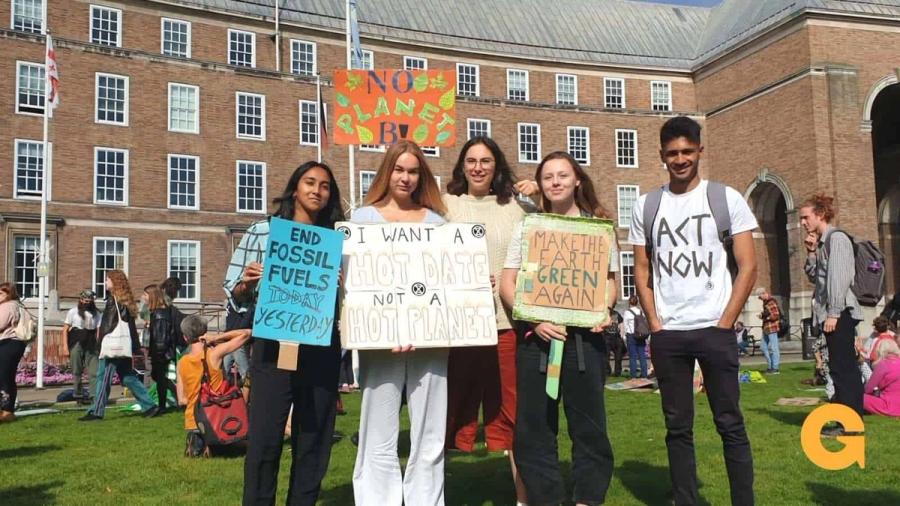 5 people are stood together holding placards and protesting for climate justice.