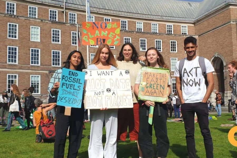 5 people are stood together holding placards and protesting for climate justice.
