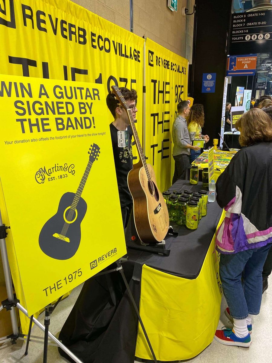 A volunteer talks to fans in REVERB's bright yellow Eco-Village at The 1975’s show in Nottingham in February 2020.