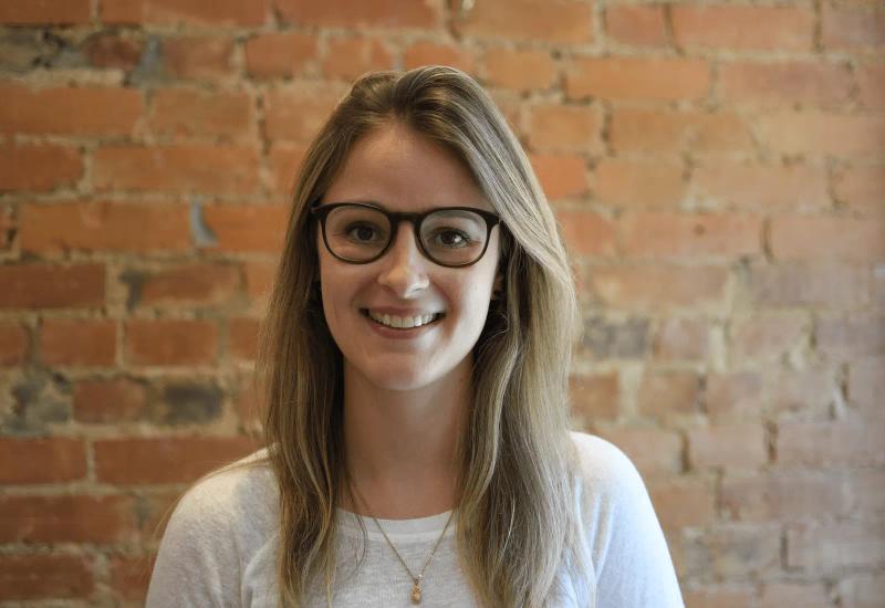 A headshot of a woman named Kate wearing glasses and a white t shirt