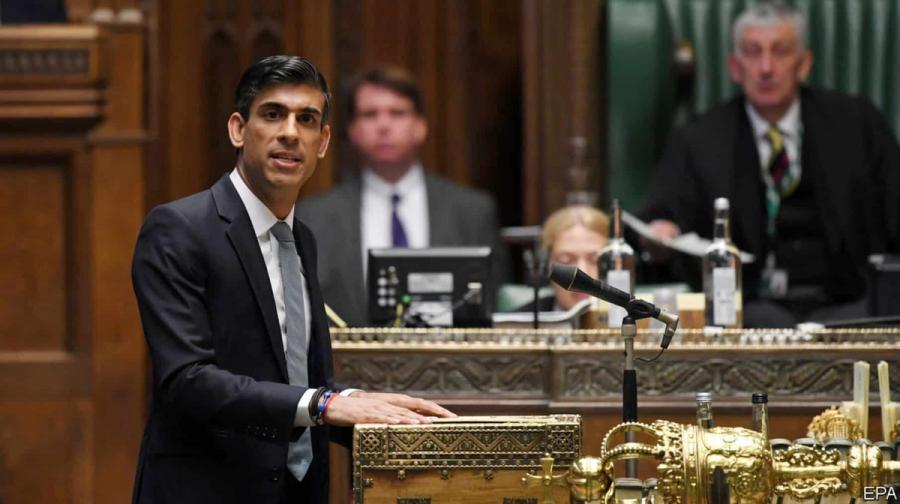 A dark skinned man in a suit stands at a microphone speaking