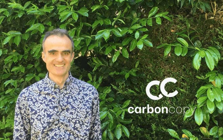 A white man wearing a blue paisley shirt stands in front of a living wall