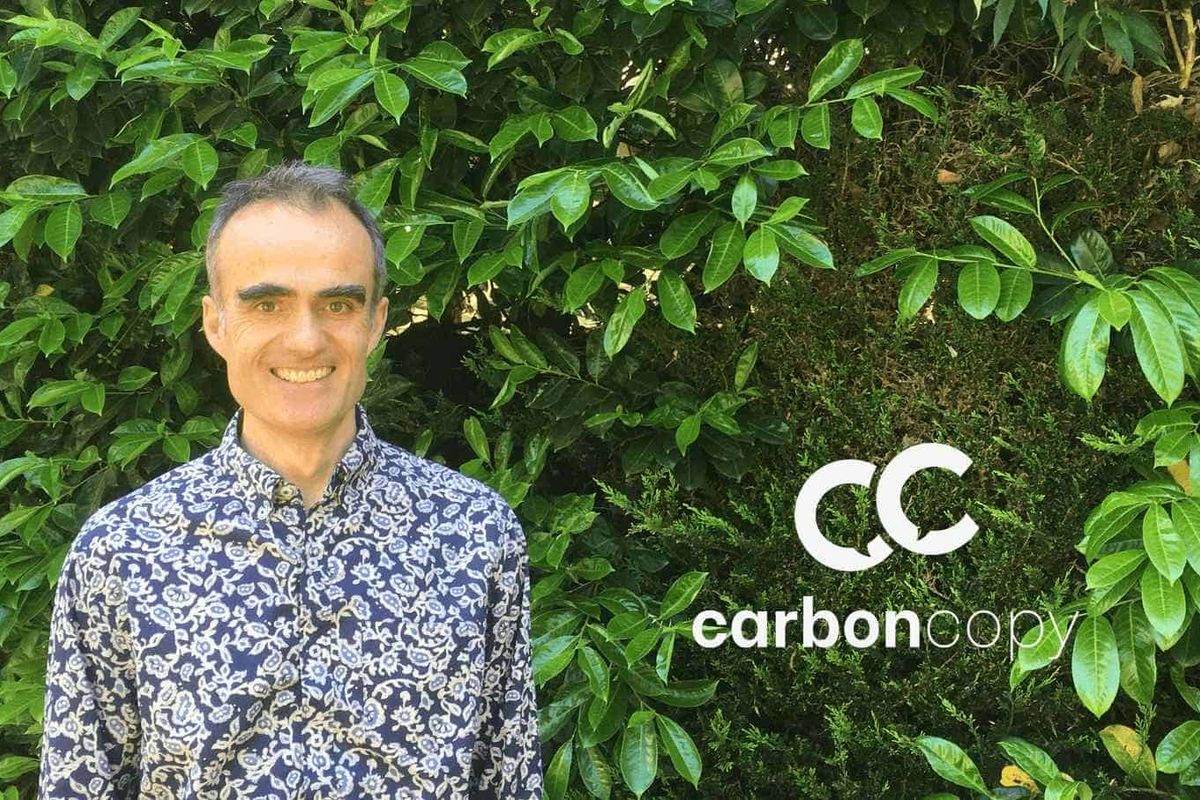 A white man wearing a blue paisley shirt stands in front of a living wall