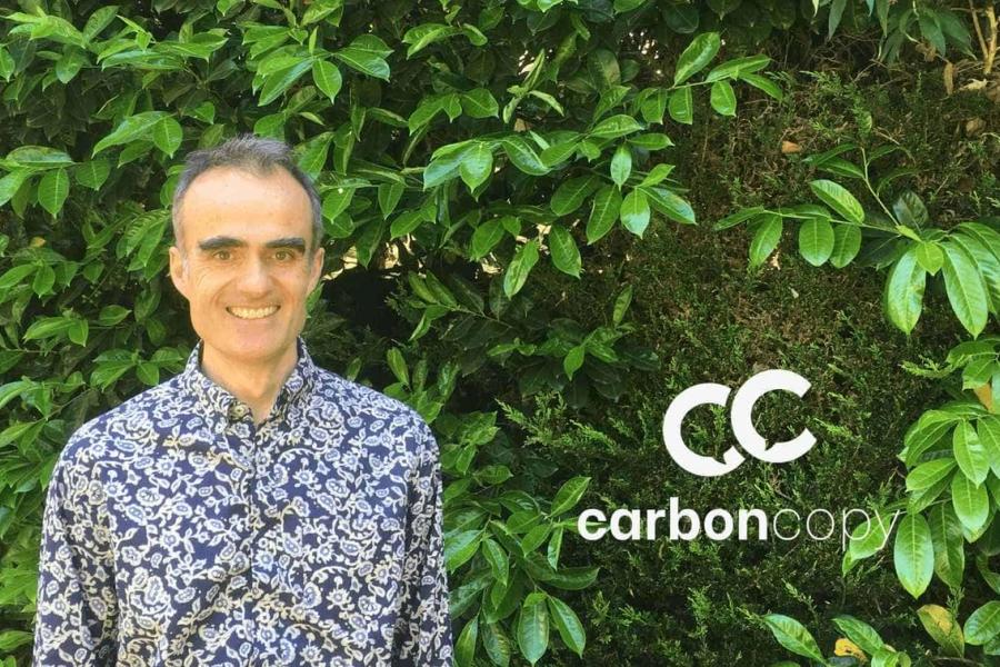 A white man wearing a blue paisley shirt stands in front of a living wall