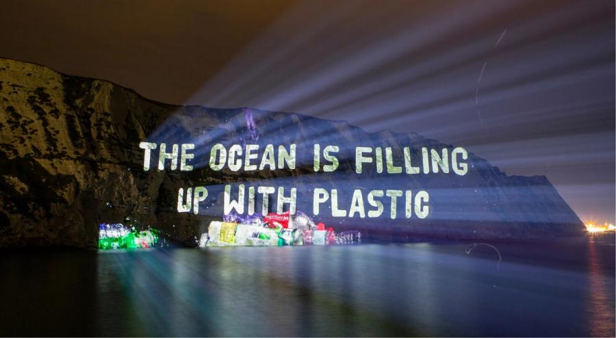 Sewage pollution protest message projected onto a coastal cliff at night.