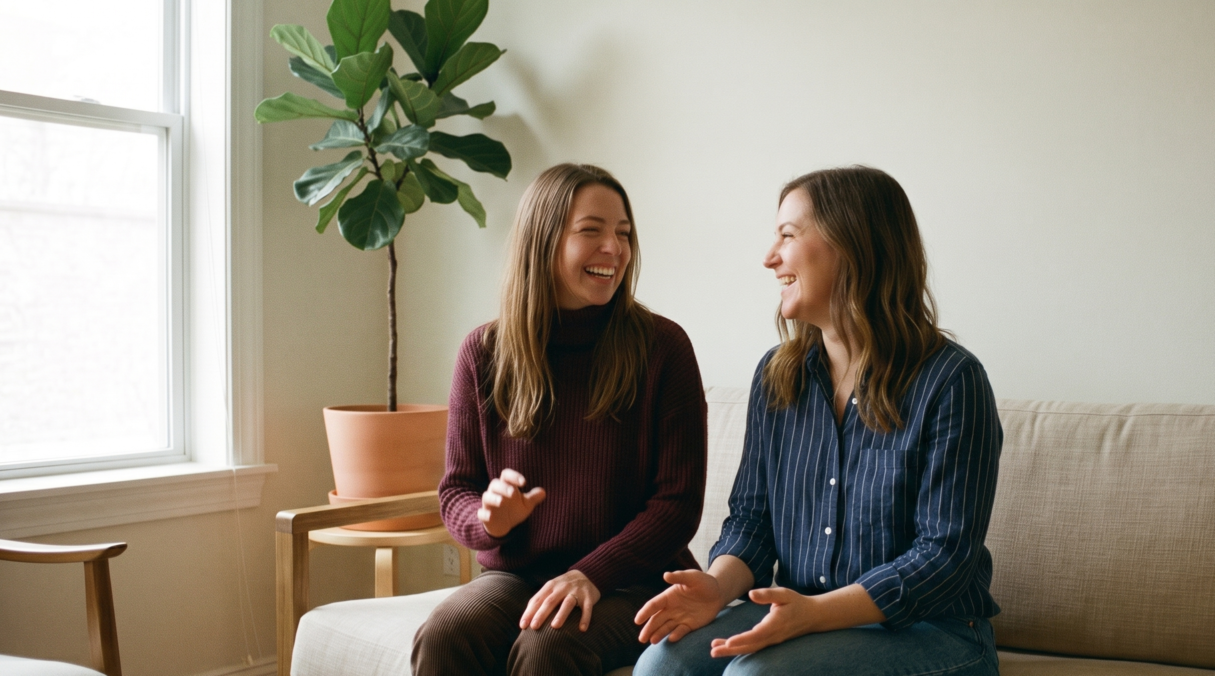 Deux amies assises côte à côte sur un canapé, en train de rire pendant leur conversation.