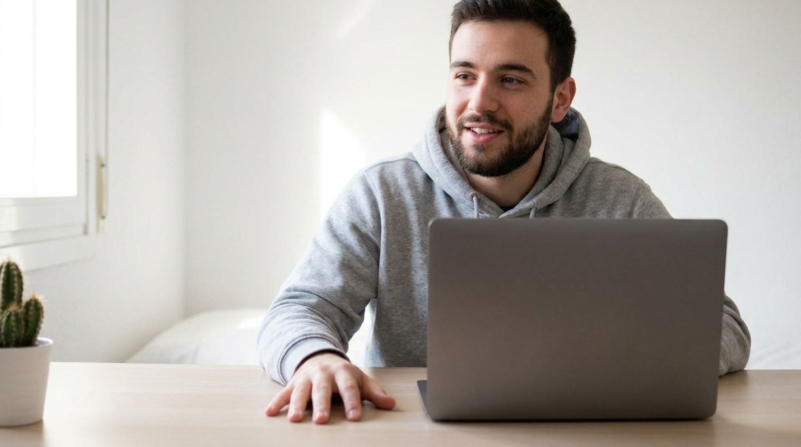 Un jeune homme en sweat gris répète sa présentation devant son ordinateur portable, la main posée sur le bureau.