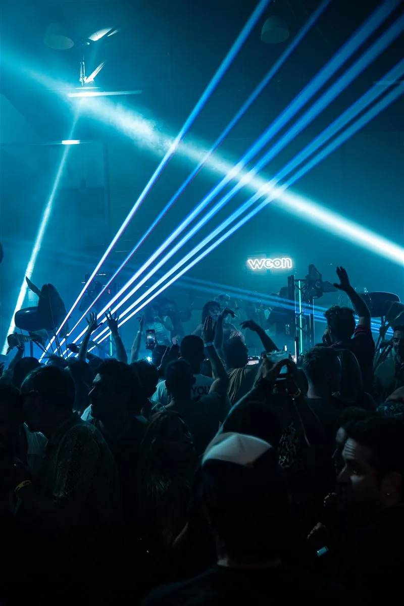 Crowd with raised hands under blue laser beams on a club night