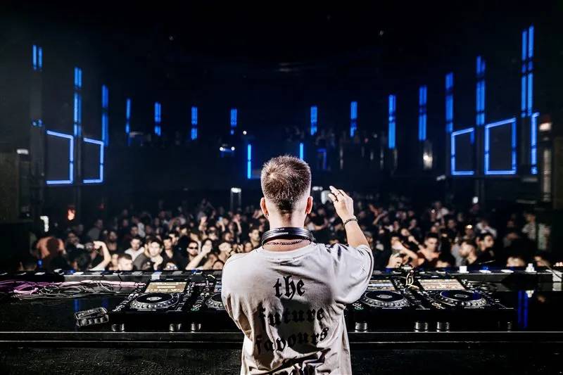 DJ seen from behind facing a packed club lit by blue panels