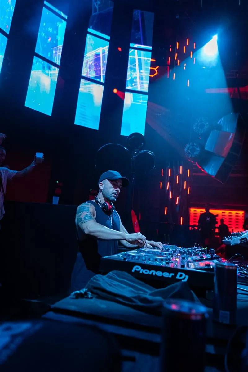 DJ in a cap at Pioneer DJ decks under blue and red light