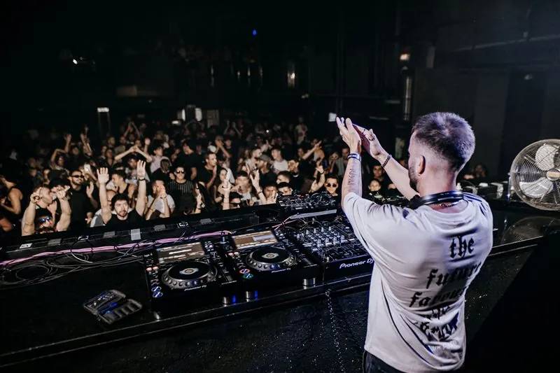 DJ clapping above the decks while the crowd raises its hands