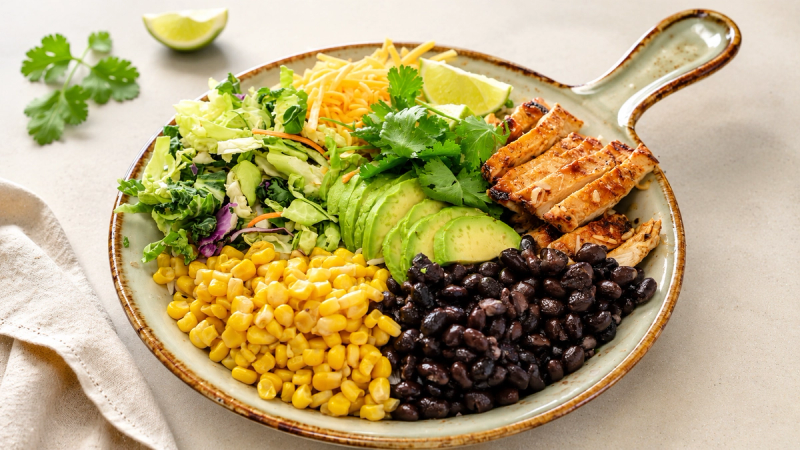 A protein bowl with grilled chicken, black beans, corn, avocado, cheddar and greens