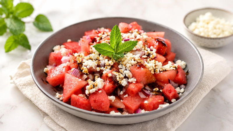 Cubed watermelon salad with crumbled feta, red onion and fresh mint in a grey bowl