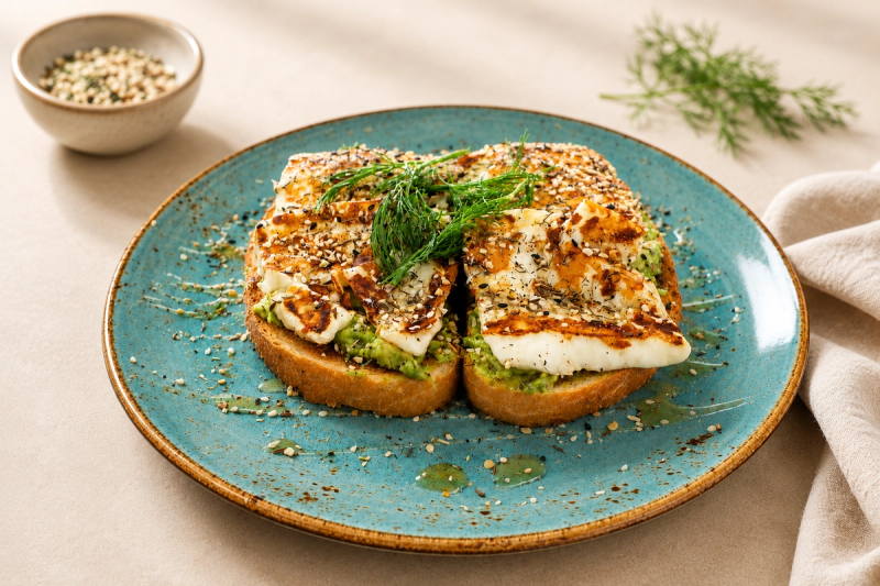 Grilled halloumi over smashed avocado on toasted sourdough, sprinkled with seeds and dill