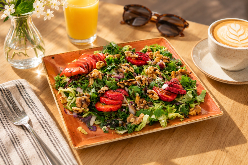 Kale salad with sliced strawberries and walnuts on a terracotta plate, with coffee and orange juice