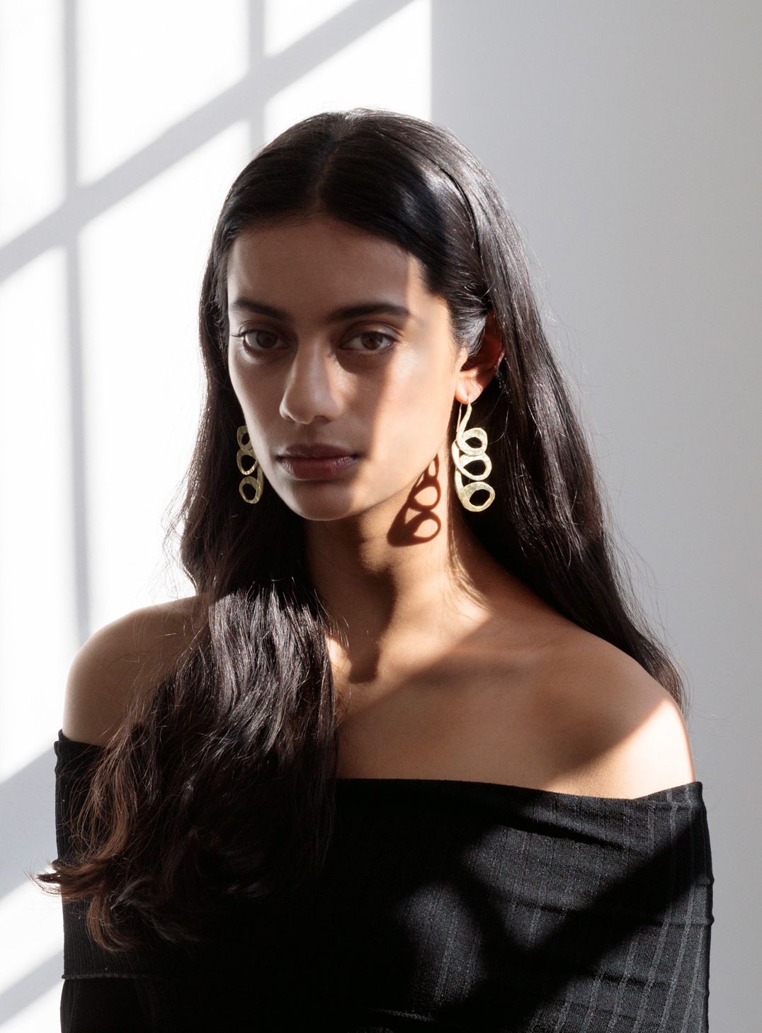 Woman modelling a black knit dress and sculptural gold earrings