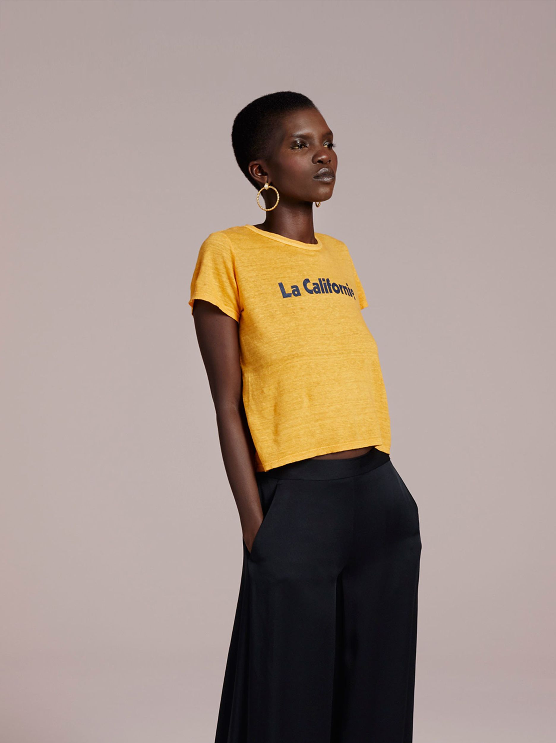 A model poses in a yellow t-shirt, black wool pants and large gold hoop earrings