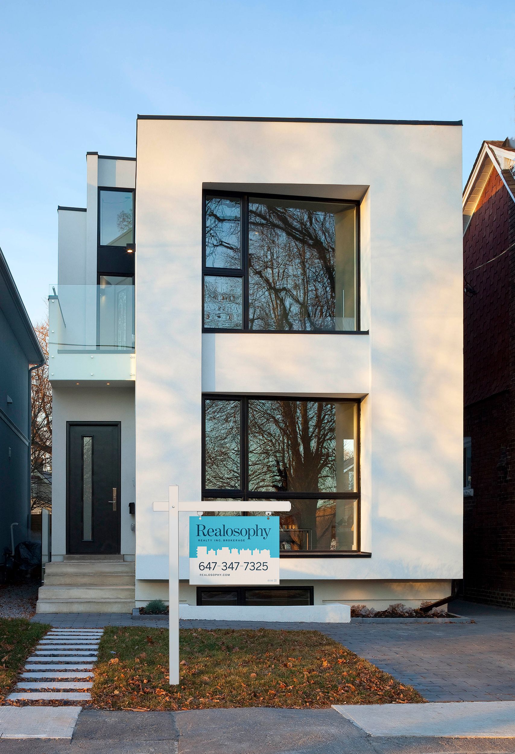 A real estate broker sign reading "Realosophy" on the lawn of a white modernist house