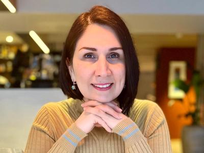 A woman sitting at a dinner table, smiling with her hands beneath her chin.