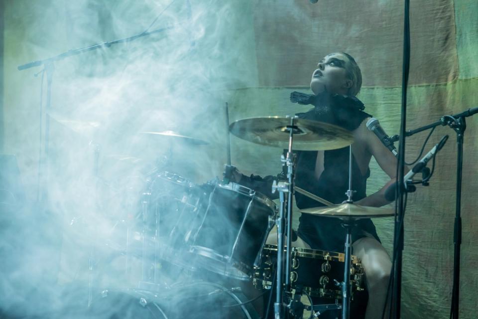 A drummer performing on stage surrounded by smoke, with intense focus and energy. The drummer is dressed in dark clothing and has a dramatic pose, playing a drum kit under dim lighting, adding to the atmospheric, electrifying vibe of the performance.*