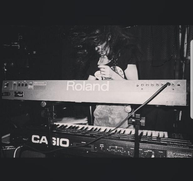 A long-haired man headbanging behind two keyboards