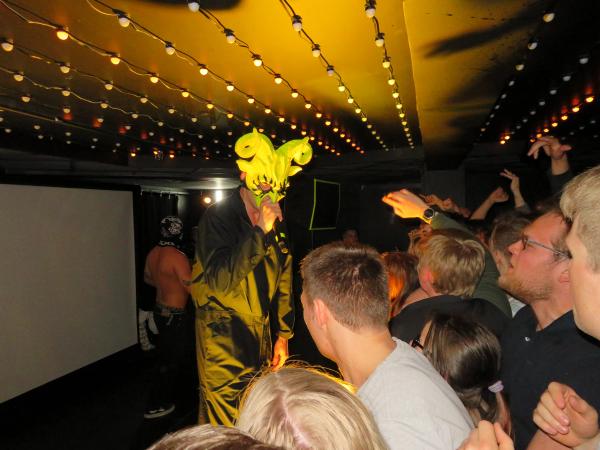 A man in a yellow mask with goat horns performing in front of an eager crowd