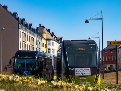 Two modern city buses in Trondheim, Norway, driving through a street lined with colorful buildings on a sunny spring day.